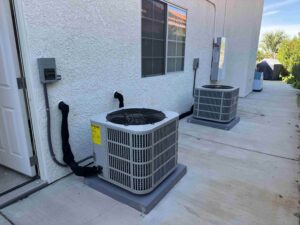 Two newly installed residential air conditioning condenser units mounted on concrete pads outside a stucco home in Palmdale, serviced by Origin Heating & Air