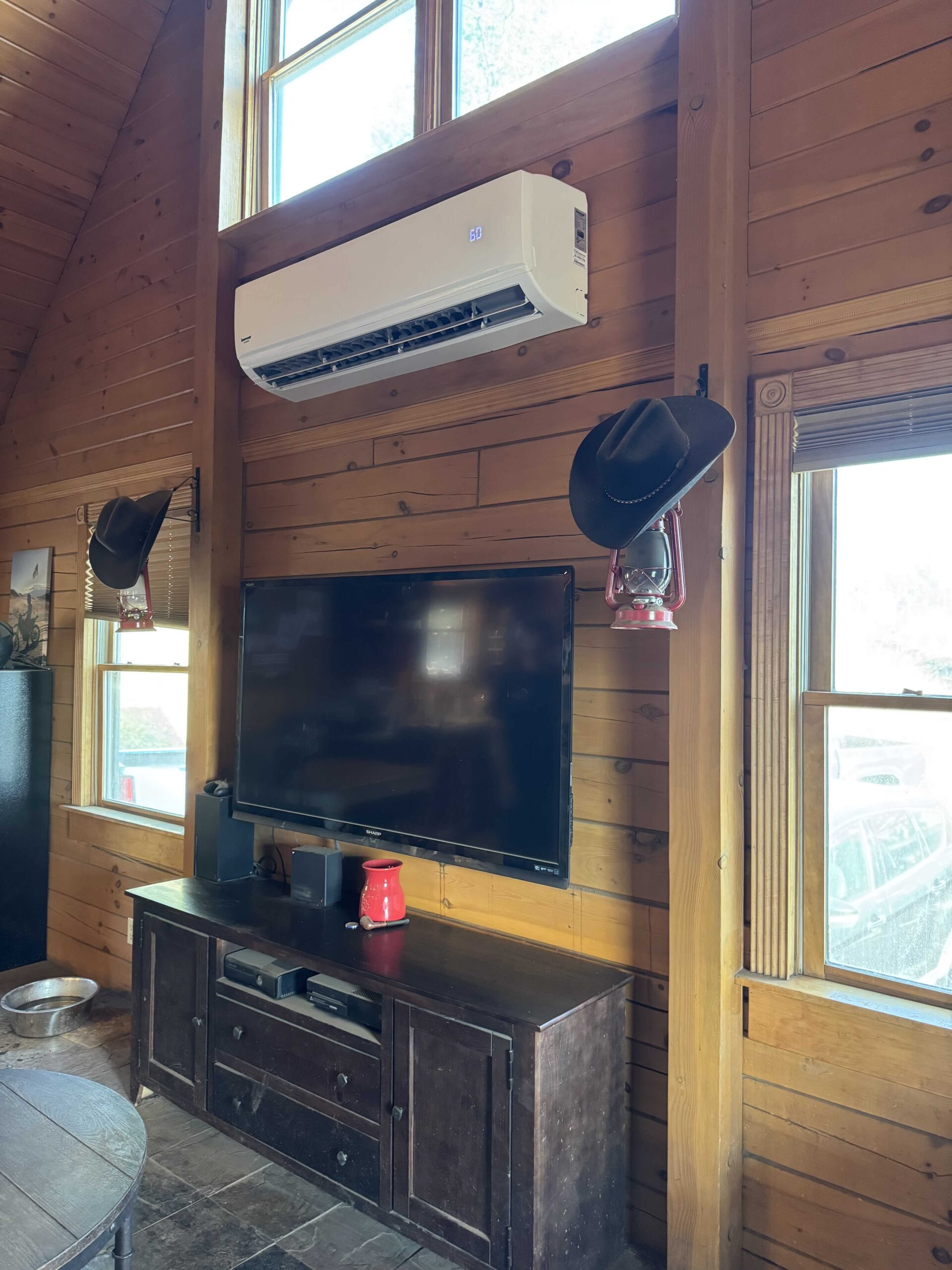 Wall-mounted ductless mini-split air conditioning unit installed in a rustic wood-paneled cabin interior, providing efficient cooling before summer