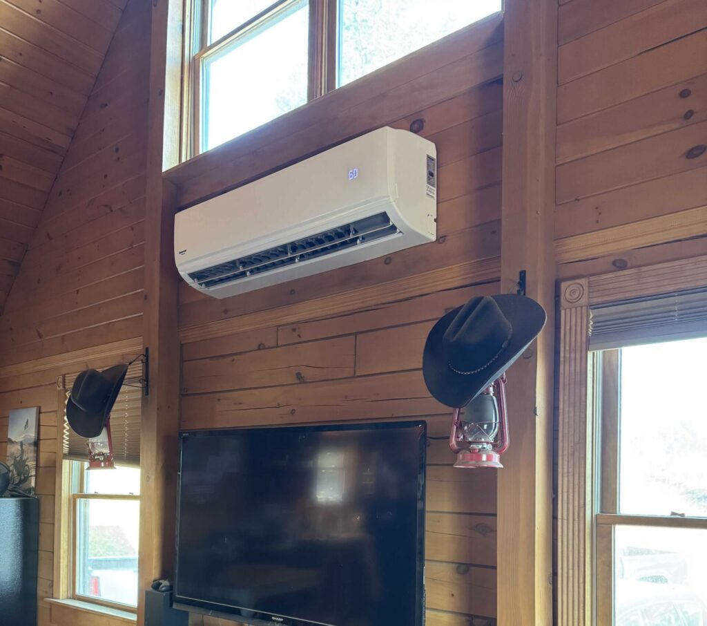 Wall-mounted ductless mini-split air conditioning unit installed in a rustic wood-paneled cabin interior, providing efficient cooling before summer