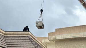 Crane lifting a new air conditioning unit onto a Palmdale rooftop during installation
