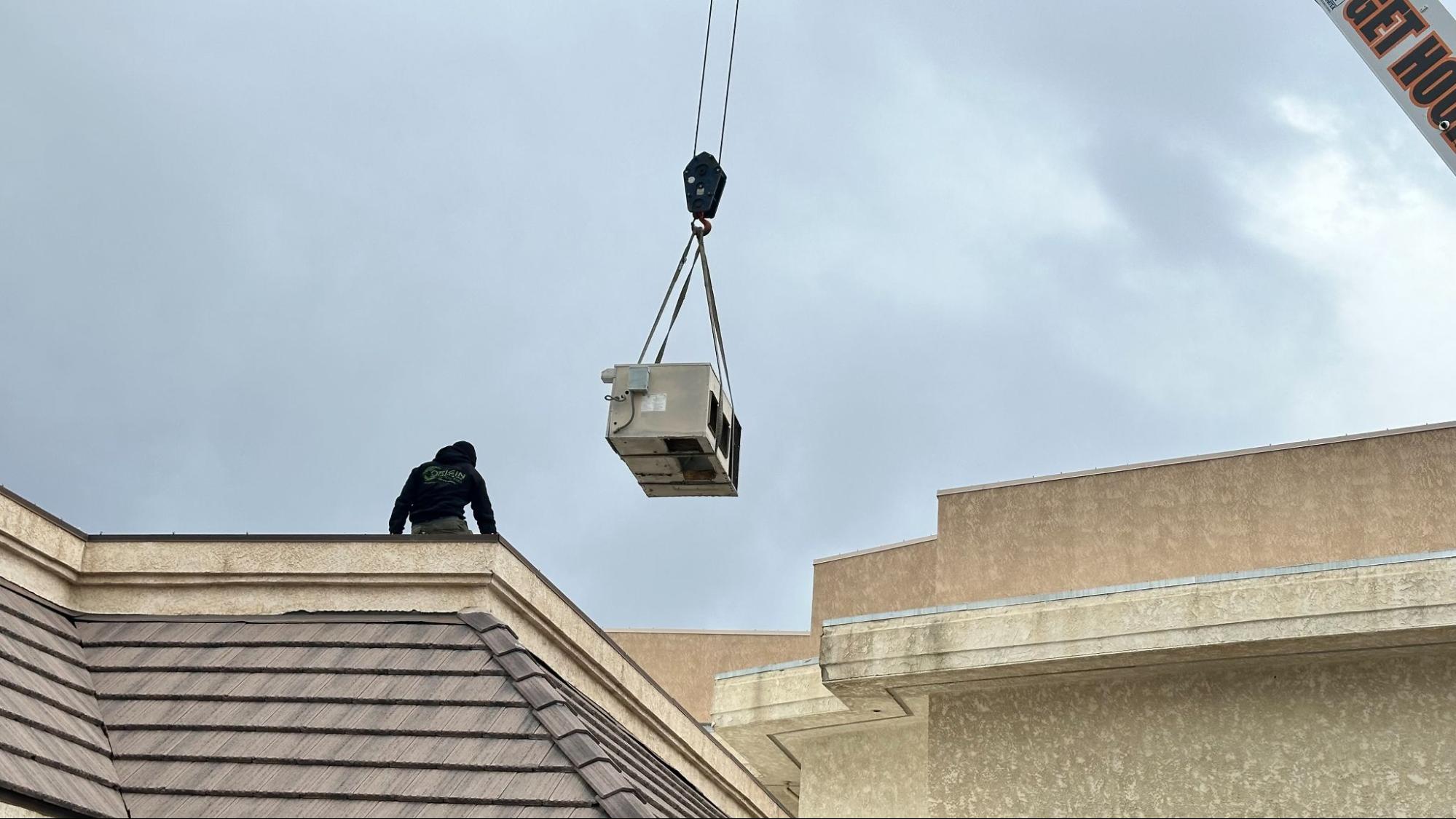 Crane lifting a new air conditioning unit onto a Palmdale rooftop during installation