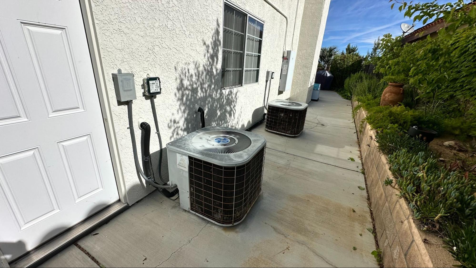 Two residential HVAC condenser units positioned along a walkway, requiring seasonal care to handle changing weather demands in Tehachapi