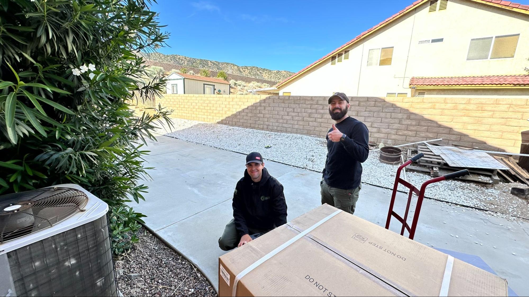 Origin Heating & Air technicians preparing to install a new outdoor HVAC unit next to the existing condenser