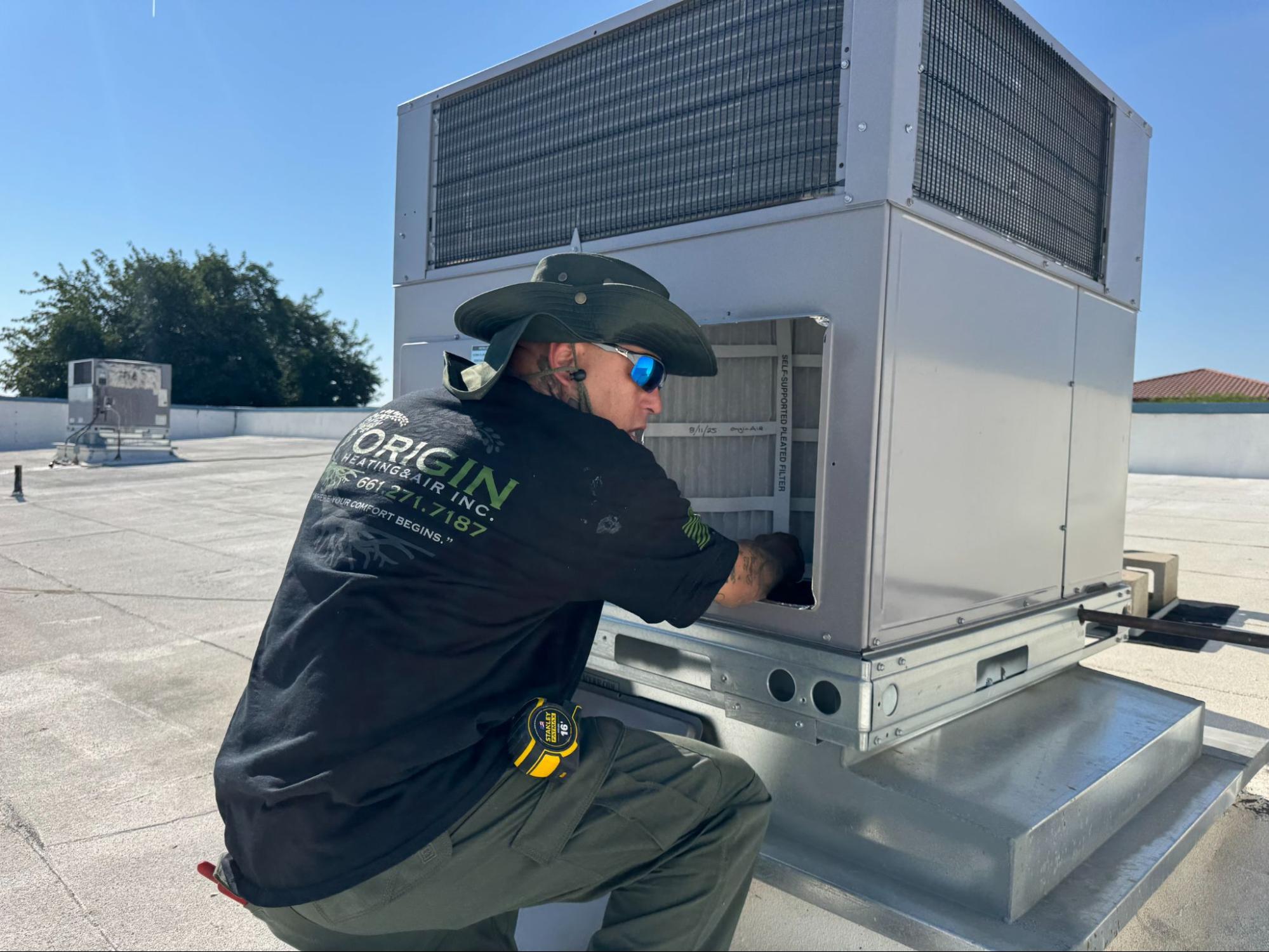 Origin Heating & Air technician inspecting a rooftop package unit's filter during AC installation