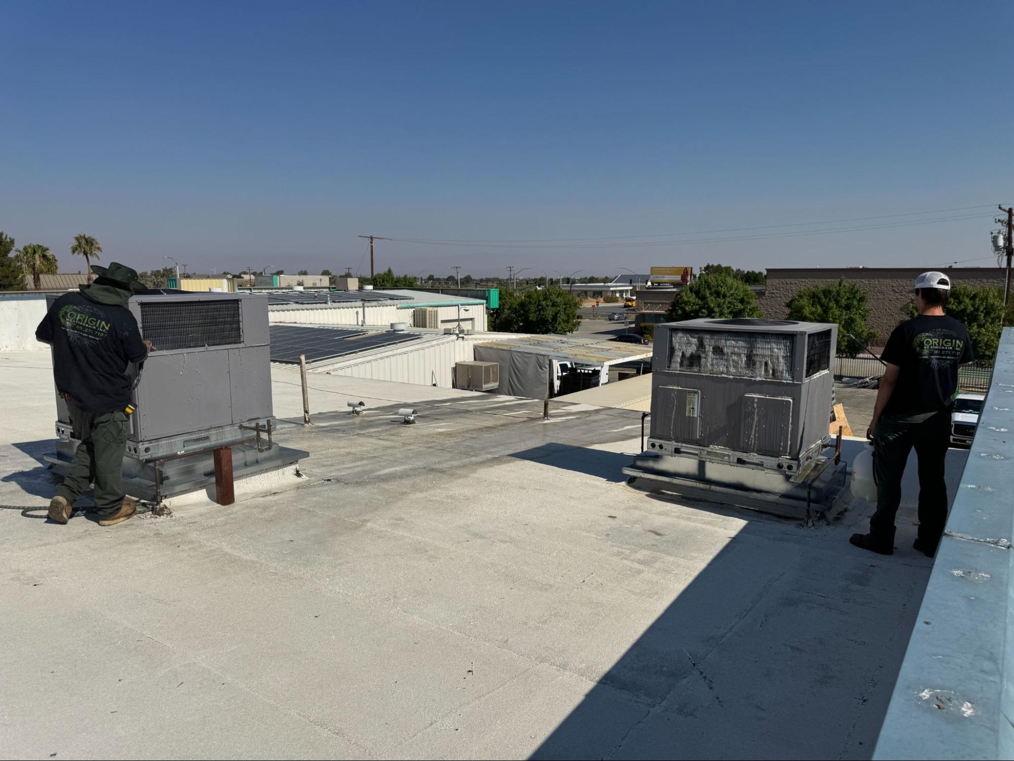 Origin Heating & Air technicians inspecting rooftop HVAC units as part of scheduled maintenance service